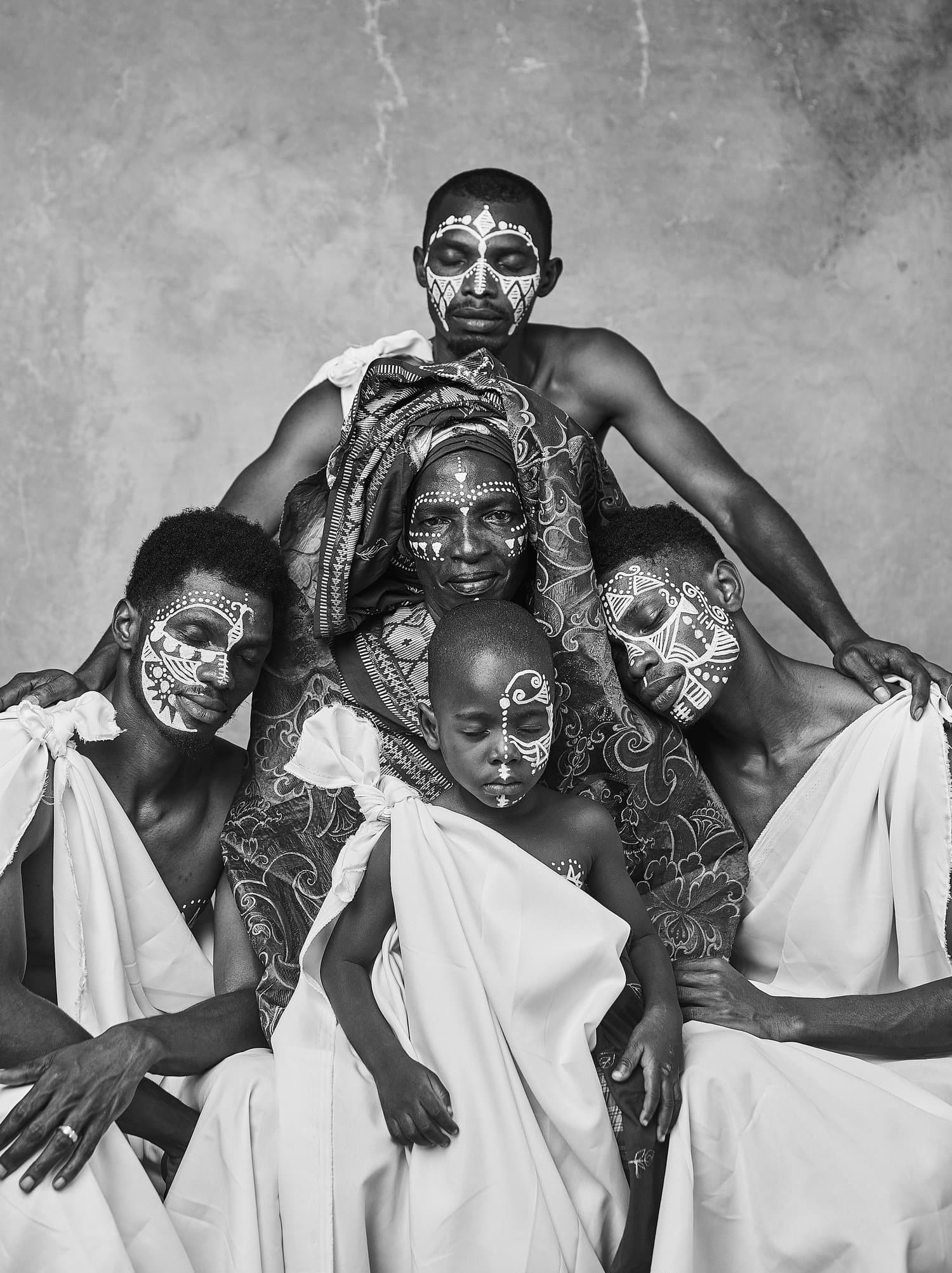 Three generations of a Black family in white cloth and traditional face paint, gathered around an elder